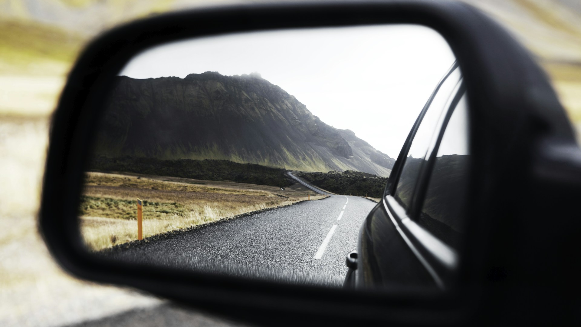 Visão de futuro: espelho retrovisor de um carro a mostrar a estrada já percorrida, com uma montanha ao fundo